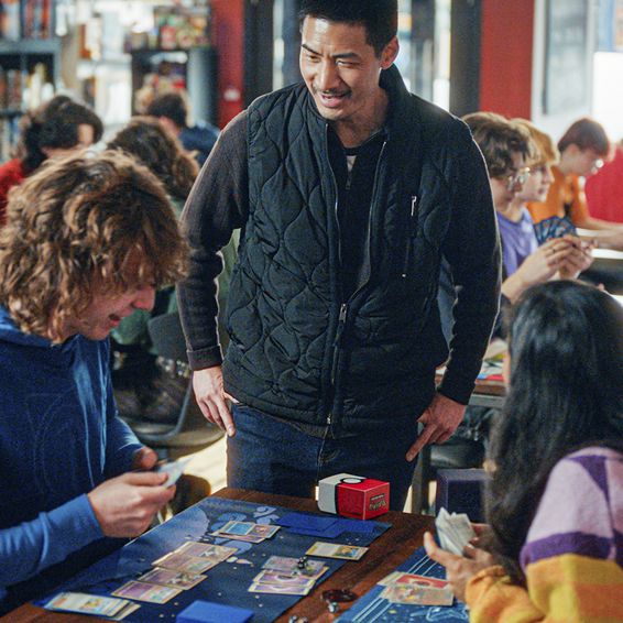 A man chatting with two people playing the Pokémon TCG.